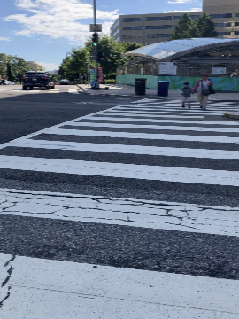A picture of the crosswalk across 7th Street. In the distance there is the canopy for the escalator entrance to the station.