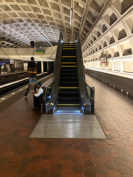 A picture of the Greenbelt side of the Upper Level platform. The train tracks are on the left and there is a half wall on the right. There is an escalator in the central background of the picture.