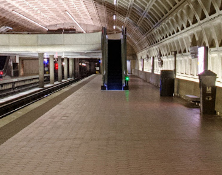 A picture of the Greenbelt side of the Upper Level platform. The train tracks are on the left and there is a half wall on the right. There is an escalator in the central background of the picture.